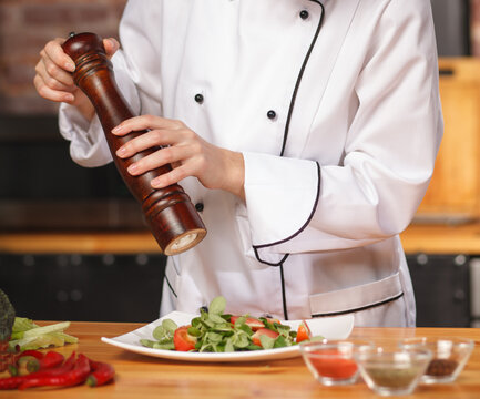 Chef adding pepper to fresh vegetable salad in kitchen. Healthy cooking and restaurant cuisine concept.
