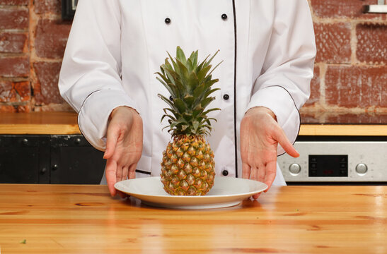 Chef presenting fresh pineapple on plate in kitchen. Tropical fruit, healthy food and culinary concept.