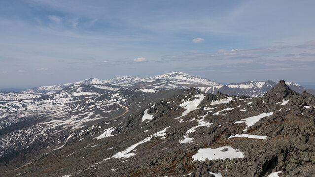 Wide panoramic view from Konzhakovsky Kamen with rocky ridge and melting snowfields in the Northern Urals, Sverdlovsk Oblast, Russia, on a clear day