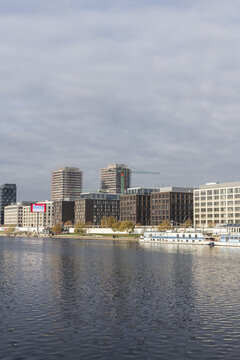 View of modern office buildings and residential towers along the Spree river with boats docked at the waterfront under a cloudy sky Berlin, Berlin, Germany.