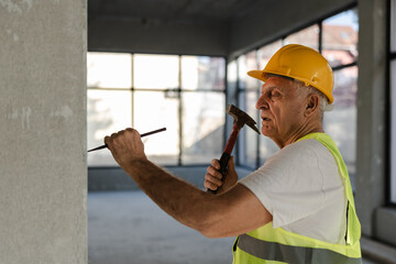 Naklejka premium Senior Worker Builds a Wall With Hammer and Chisel in a Construction Site During Daytime