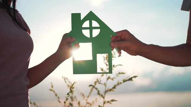 Family mortgage concept. Family holds paper house with their hands at sunset. Family house on loan. Paper house is symbol of family happiness.Housing and mortgage crisis.Dream concept of buying house