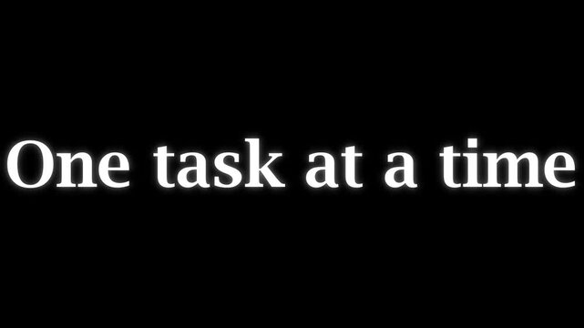 Minimalist typography text animation featuring repeated phrase one task at a time with particle dispersion effect on a solid pitch black background motion graphic