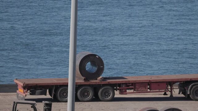 Large metal cylinder on flatbed truck near water at shipping dock in the afternoon