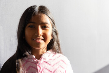Indian child facing lens smiling wearing pink zipup fleece sun lighting face shadow on gray wall © wavebreak3
