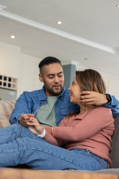 Couple sitting on sofa in modern home, holding hands, showing smartwatch, coffee table
