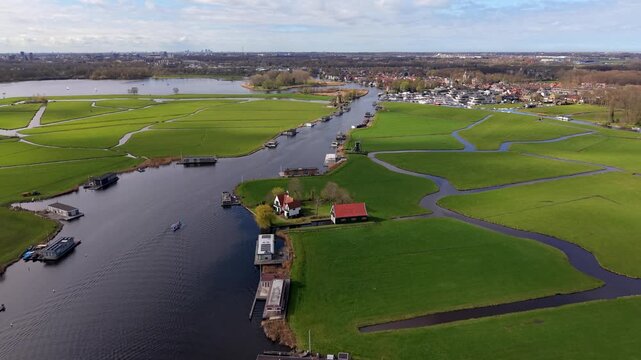 Stunning aerial view of the Dutch polder landscape featuring lush green fields, winding canals with houseboats, and traditional windmills under a cloudy sky in the Netherlands countryside.