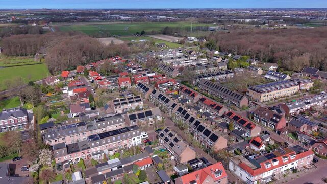 Aerial drone view of a sustainable Dutch neighborhood with solar panels on rooftops, red brick houses, and green surroundings. High angle perspective of a modern residential area in the Netherlands.