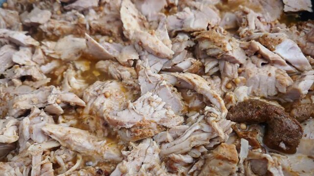 Shredded cooked meat in a pan with visible spices and juices, showcasing the texture and color of the dish in a close-up view, highlighting culinary preparation details
