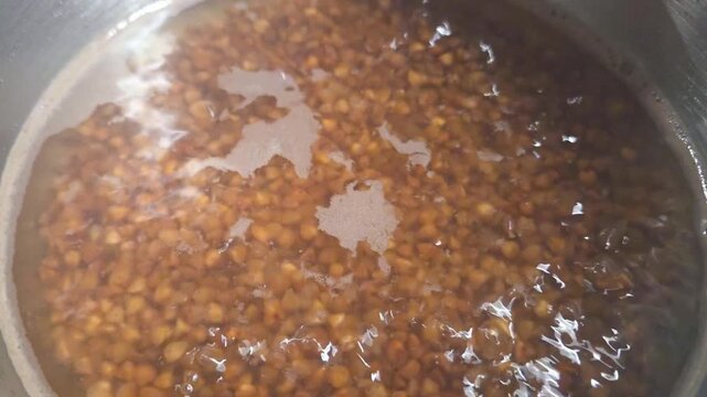 Close-up of boiling grains in a pot with water, showcasing the gradual softening and color change of the grains during the cooking process in a kitchen setting
