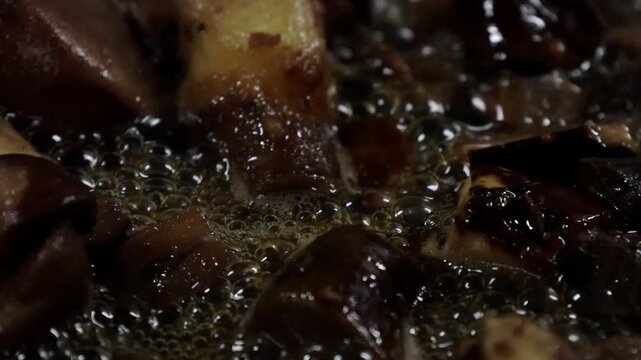 Cooking process of diced meat pieces frying in hot oil, bubbles forming around the food in a frying pan, creating a rich and flavorful dish