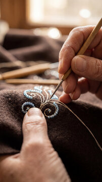 Detailed view of hands embroidering brown fabric with blue glass beads using a hook. Traditional handicraft, artisan beading process, textile art.