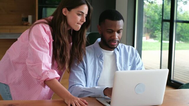 Professional diverse colleagues working on a business project, with a female manager mentoring a male employee while pointing at the laptop screen in a modern office or home office setting