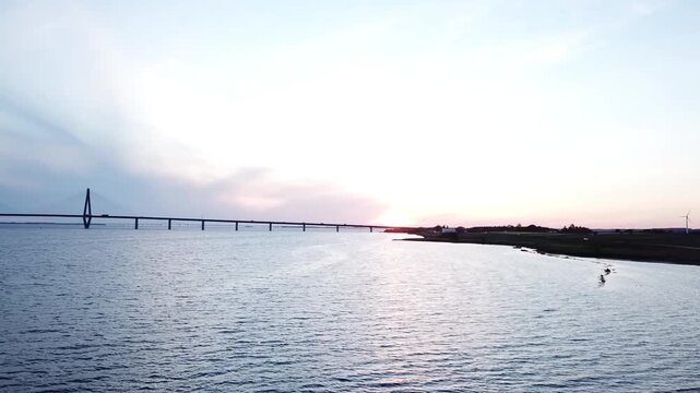 Drone video capturing the golden setting sun over the Far&oslash; peninsula in Denmark, with cars moving along the roads below. The sweeping footage also reveals the scenic bridge connecting Far&oslash; to Havns&oslash;
