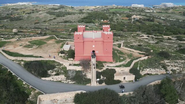 Cinematic aerial drone shot of the historic Saint Agatha's Red Tower surrounded by Mediterranean vegetation in Mellieha, Malta.
