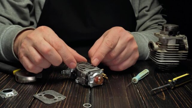 Hands of a mechanic assembling small engine components on a wooden workbench with various tools and parts arranged around the workspace