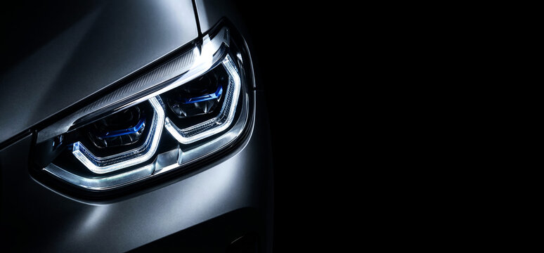 Modern luxury car LED headlight closeup with double U-shaped DRL and blue projectors on black background