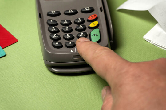A person is using their finger to press a button on a card reader device. This action takes place during a payment process in a shop setting