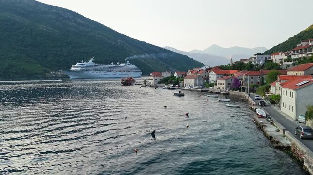 Royal Caribbean cruise ship sailing past a waterfront village along a coastal road, Bay of Kotor, June 2025