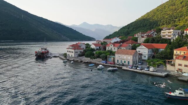 Aerial view of a small coastal village with red roofs and a wooden tourist boat in a deep mountain bay