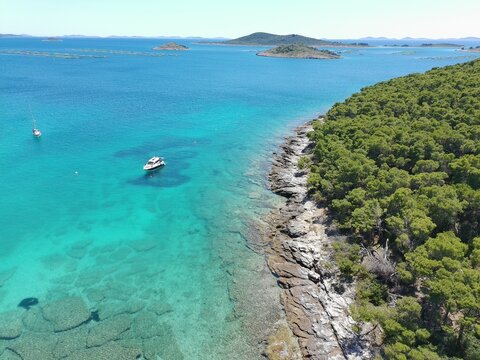 Adriatic sea rocky coastline with cleen turqouise sea and boats in the distance, aerial photo