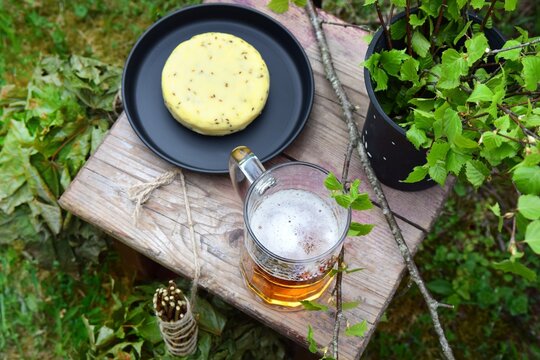 Traditional Latvian caraway cheese and beer on a wooden stool with fresh birch branches in a black ceramic vase from a high angle