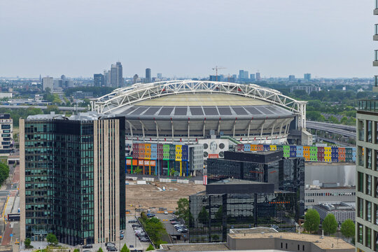 Amsterdam, Netherlands, May 08, 2026. High angle view of the Johan Cruijff Arena stadium roof and surrounding colorful buildings with a large urban construction site in the foreground.