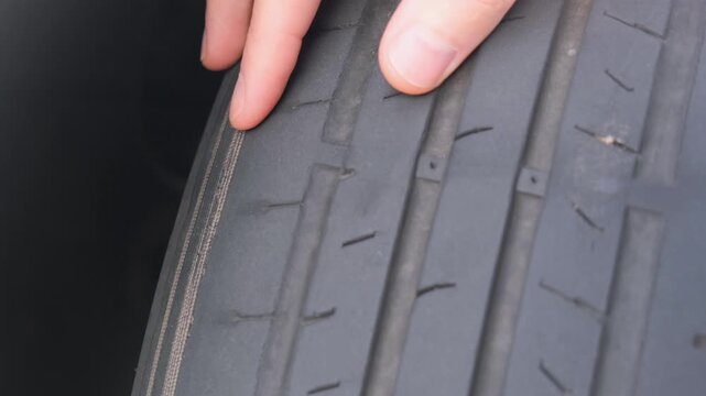 Close-up of a hand checking the worn and cracked rubber tread of an old car tire