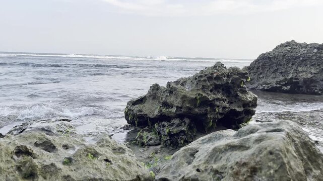 Overcast day at a rugged rocky coastline where dark, ancient stones stand resilient against the relentless push and pull of powerful ocean waves, capturing nature's raw, untamed beauty