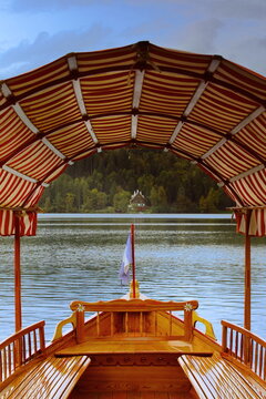 Colorful, striped awning of a modern pletna (wood rowboat) moored at Mlino port frames a stately villa on the Lake Bled north shore. Bled-Slovenia-026