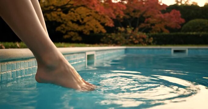 Woman's feet dipping in a clear villa pool with a warm autumn garden backdrop.