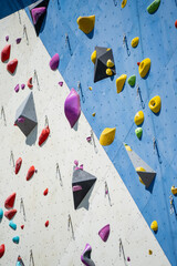 Naklejka premium Vibrant collection of ergonomic bouldering holds and technical safety carabiners installed on a dual tone geometric climbing wall for professional athletic training and hobby