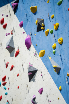 Vibrant collection of ergonomic bouldering holds and technical safety carabiners installed on a dual tone geometric climbing wall for professional athletic training and hobby