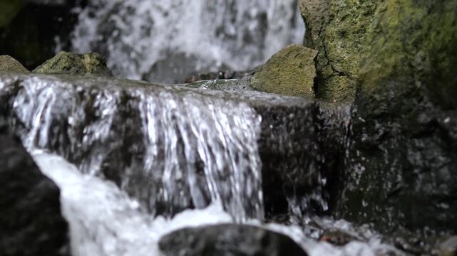 Crystal clear water of a mountain stream cascading over dark, mossy stones in a tranquil forest. The peaceful sound and sight of the flowing water creates a relaxing and natural ambiance
