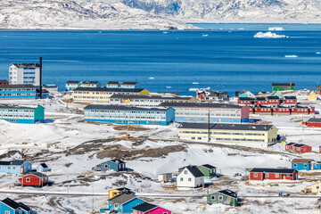 Colorful downtown of arctic settlement with Inuit houses and blocks scattered across snow hills on the coast of winter fjord full of icebergs, Narsaq, Kujalleq municipality, Greenland © vadim.nefedov