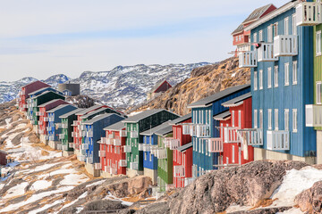 Obraz premium Dense urban housing in a Greenlandic town with colorful facades, white balconies, and snow arctic hills rising behind, Qaqortoq, Kujalleq municipality, Greenland.