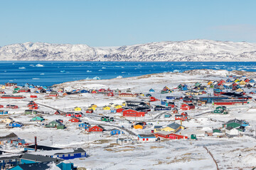 Colorful downtown of arctic settlement with Inuit houses scattered across snowy hills on the coast of winter fjord full of icebergs, Narsaq, Kujalleq municipality, Greenland © vadim.nefedov