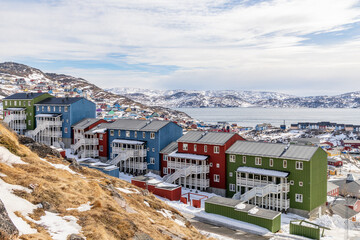 Obraz premium Colorful Inuit living houses standing on rocky hills with snow mountains and arctic fjord in the background, Qaqortoq, Kujalleq municipality, Greenland.
