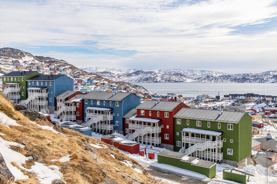 Colorful Inuit living houses standing on rocky hills with snow mountains and arctic fjord in the background, Qaqortoq, Kujalleq municipality, Greenland.