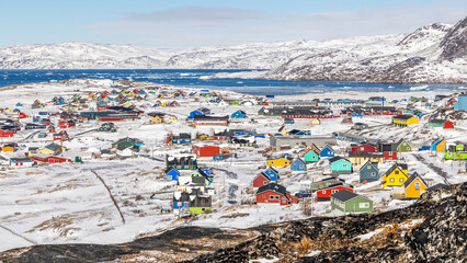 Colorful downtown of arctic settlement with Inuit houses scattered across snowy hills on the coast of winter fjord full of icebergs, Narsaq, Kujalleq municipality, Greenland © vadim.nefedov