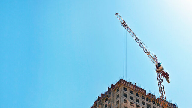 Construction crane lifting materials at a high-rise building under construction against a clear blue sky, showcasing modern architecture and urban development, copyspace