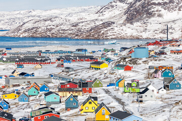 Colorful downtown of arctic settlement with Inuit houses and homes scattered across snow hills on the coast of winter lagoon full of icebergs, Narsaq, Kujalleq municipality, Greenland © vadim.nefedov