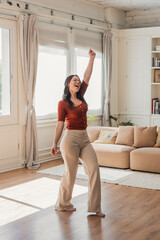 Happy young woman joyfully dancing and singing with raised arm, feeling freedom and positive...