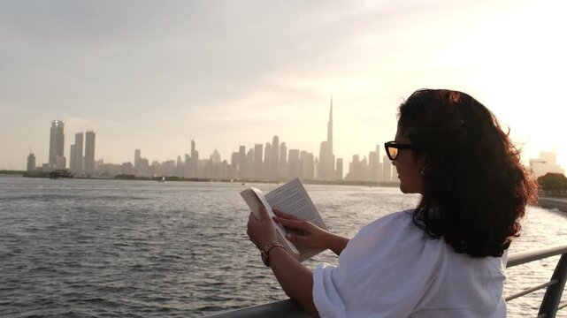 Modern woman enjoying outdoor reading and self reflection with Dubai skyline at golden hour