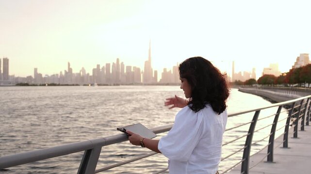 Woman freelancer talking to client on digital tablet from Dubai waterfront location