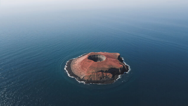 広い海の余白に小さな火山島が静かに浮かぶ空撮写真