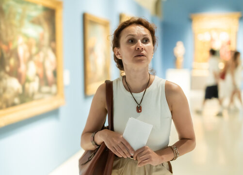 Attractive woman holding guide book in light museum of arts and admiring works of art