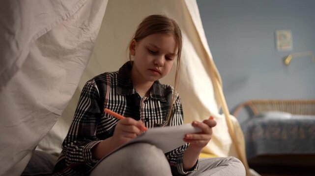 White girl writing in teepee with notebook, concentrated expression while sketching and doing homework, pen strokes on paper, bedside lamp glow, creative study .