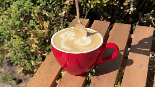 stirred with a spoon Coffee delight. Woman tasting cup of latte in cafe. Red mug full of creamy foamy cappuccino