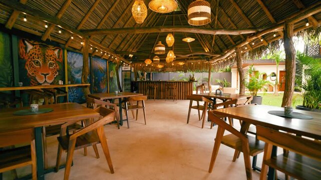 Cozy interior of an empty tropical style hotel restaurant. Rustic wooden tables and chairs under a thatched roof with warm decorative lights